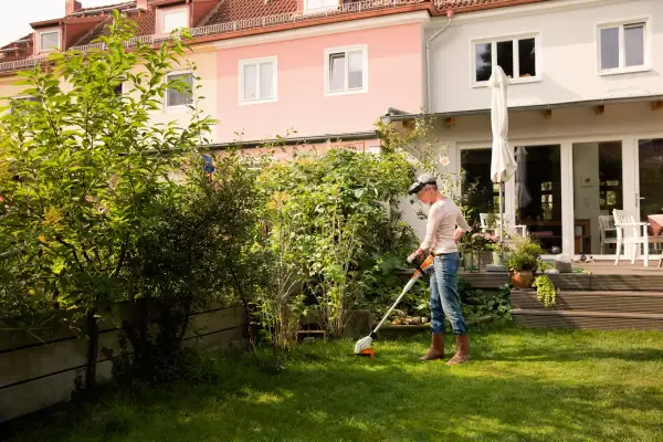 Person using a STIHL battery line trimmer along a garden bed in a back garden