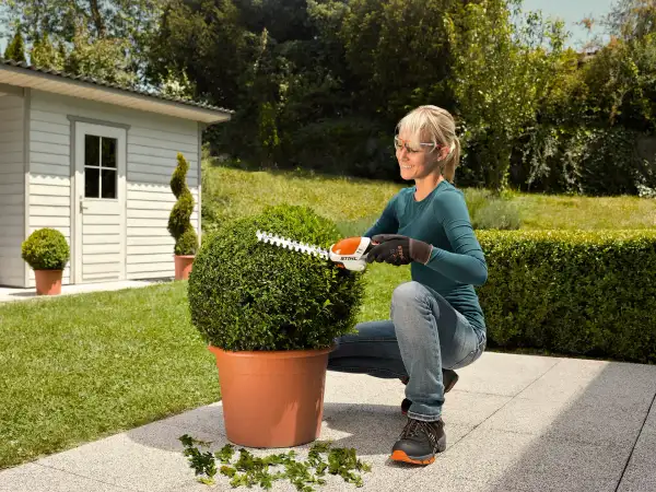 Gardener shaping a round potted shrub on a patio with STIHL battery shrub shears