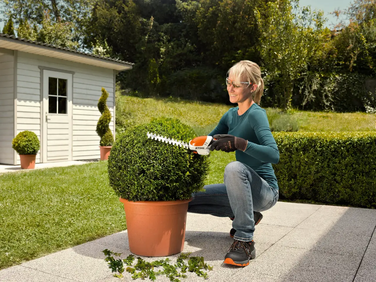 Gardener shaping a round potted shrub on a patio with STIHL battery shrub shears