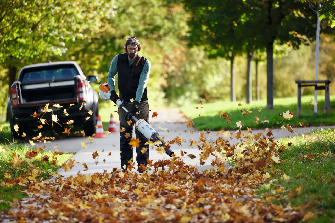 Man clearing leaves from a park path using a STIHL battery KombiSystem motor with a blower attachment